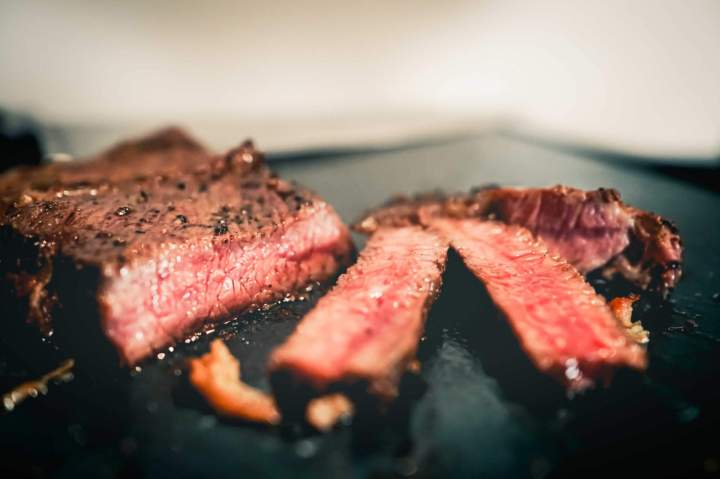 Gros plan sur un steak juteux avec des marques de grill, arrosé dune sauce, garniture fraîche, lumière chaude, photo culinaire.